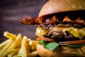 Craft beef burger with cheese, bacon, rocket leafs, caramelize onion and french fries on wood table and rustic background