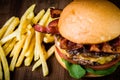 Craft beef burger with cheese, bacon, rocket leafs, caramelize onion and french fries on wood table and rustic background