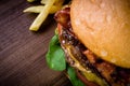 Craft beef burger with cheese, bacon, rocket leafs, caramelize onion and french fries on wood table and rustic background