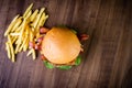 Craft beef burger with cheese, bacon, rocket leafs, caramelize onion and french fries on wood table and rustic background