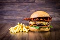 Craft beef burger with cheese, bacon, rocket leafs, caramelize onion and french fries on wood table and rustic background