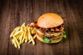 Craft beef burger with cheese, bacon, rocket leafs, caramelize onion and french fries on wood table and rustic background