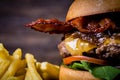 Craft beef burger with cheese, bacon, rocket leafs, caramelize onion and french fries on wood table and rustic background