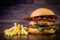 Craft beef burger with cheese, bacon, rocket leafs, caramelize onion and french fries on wood table and rustic background