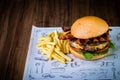 Craft beef burger with cheese, bacon, rocket leafs, caramelize onion and french fries on wood table and rustic background