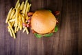 Craft beef burger with cheese, bacon, rocket leafs, caramelize onion and french fries on wood table and rustic background