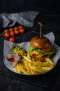Craft beef burger and french fries on wooden board on black background. Close-up. Royalty Free Stock Photo