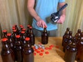 Craft beer brewing at home, man closes brown glass beer bottles with plastic capper on wooden table with red crown caps. Royalty Free Stock Photo