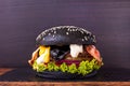 Craft black beef burger with black cheese, bacon, vegetables, onion jam, arugula on a board with a stone and wooden deck Royalty Free Stock Photo