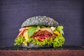Craft black beef burger with mozzarella, bacon, vegetables, onion jam, arugula on a board with a stone and wooden deck Royalty Free Stock Photo