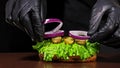 Craft burger is cooking on black background. Consist: sauce salsa, lettuce, red onion, pickle, cheese, chilli green