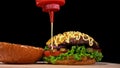 Craft burger is cooking on black background. Consist: sauce, lettuce, tomato, red onion, pickle, cheese, bacon, air bun Royalty Free Stock Photo