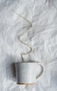 Craft ceramic mug with sand texture with brown wire as coffee smoke on white crumpled paper, handmade craft pottery, background