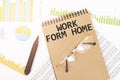 In a craft colour notebook is a WORK FROM HOME inscription, next to pencils, glasses, graphs and diagrams