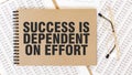 Craft colour notepad with text SUCCESS IS DEPENDENT ON EFFORT. Notepad with eyeglasses and text documents. Business concept Royalty Free Stock Photo