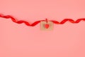 craft envelope with red heart attached to a swirling red ribbon isolated on a pastel pink background