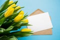 A craft envelope and a white paper on a blue background with bouquet of yellow tulips. The concept of spring holidays: Easter, Royalty Free Stock Photo