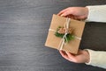 Craft gift of brown paper with twigs of Christmas tree and twine in the hands of a girl