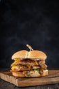 Craft juicy double burger with delicate meat cutlet on wooden cutting board on a smoky black background