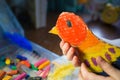 Craft with kids. bright bird, cut from cardboard and painted with wax crayons,in the hands of a child