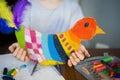 Craft with kids. bright bird, cut from cardboard and painted with wax crayons,in the hands of a child