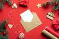 Craft paper envelope with empty card inside and Christmas decorations, gifts, fir tree branches on red background. Christmas Royalty Free Stock Photo