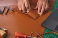 Craftsman gluing leather wallet in workshop with tools and laptop Royalty Free Stock Photo