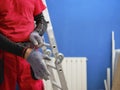 Craftsman holding a saw ready to perform home renovation. Worker in work clothes on a construction site on an aluminum folding Royalty Free Stock Photo