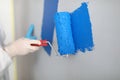 Craftsman holds roller and paints white wall blue.