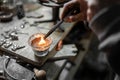 A craftsman jeweler is pouring some melted silver in a mold to make an unique piece