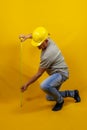 Craftsman worker with hard hat is measuring with a tape measure isolated on yellow background Royalty Free Stock Photo