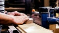 Craftsman working with grinding machine at wood workshop, hands closeup.