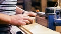 Craftsman working with grinding machine at wood workshop, hands closeup.