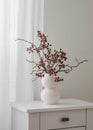 Cranberry branches in a white ceramic vase in Scandinavian style on a white wooden chest of drawers