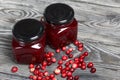 Cranberry jam in glass jars. Cranberries are scattered nearby. On wooden boards with a beautiful texture