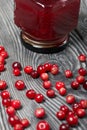 Cranberry jam in glass jars. Cranberries are scattered nearby. On wooden boards with a beautiful texture