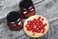 Cranberry jam in glass jars. Nearby are cranberries in a wooden saucer. On wooden boards with a beautiful texture