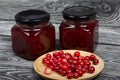 Cranberry jam in glass jars. Nearby are cranberries in a wooden saucer. On wooden boards with a beautiful texture