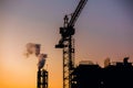 Crane and building construction site with pipe with smoke on background of sunset sky. Industrial landscape with silhouettes of c Royalty Free Stock Photo