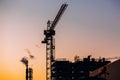 Crane and building construction site with pipe with smoke on background of sunset sky. Industrial landscape with silhouettes of c Royalty Free Stock Photo