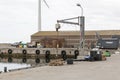 A crane at the harbor to lift fish boxes from boats and up on land, fish boxes stand next to it, a number of euro pallets can be