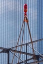 Crane hoisting block with hook on steel chain on steel rope. Glass facade of a modern skyscraper in the background. Loading\