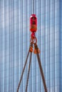Crane hoisting block with hook on steel chain on steel rope. Glass facade of a modern skyscraper in the background. Loading\