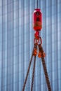 Crane hoisting block with hook on steel chain on steel rope. Glass facade of a modern skyscraper in the background. Loading\