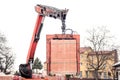 Crane or industrial forklift delivers a brick pallet at building construction site, isolated on white sky