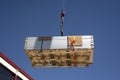 A crane lifts a stack of solar panels to the roof for installation.