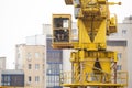 Crane operator in action. He sits on top of the crane cabin and works. Houses and windows are visible around