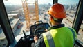 Crane operator in reflective vest and helmet inside cab. Panoramic view of construction site below. Man controls heavy machinery, Royalty Free Stock Photo