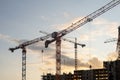 Cranes loom at a construction site against a colorful sunset, as workers engage in various tasks to progress the Royalty Free Stock Photo