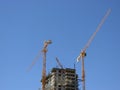 Cranes and under-construction apartment building against blue sky. Royalty Free Stock Photo